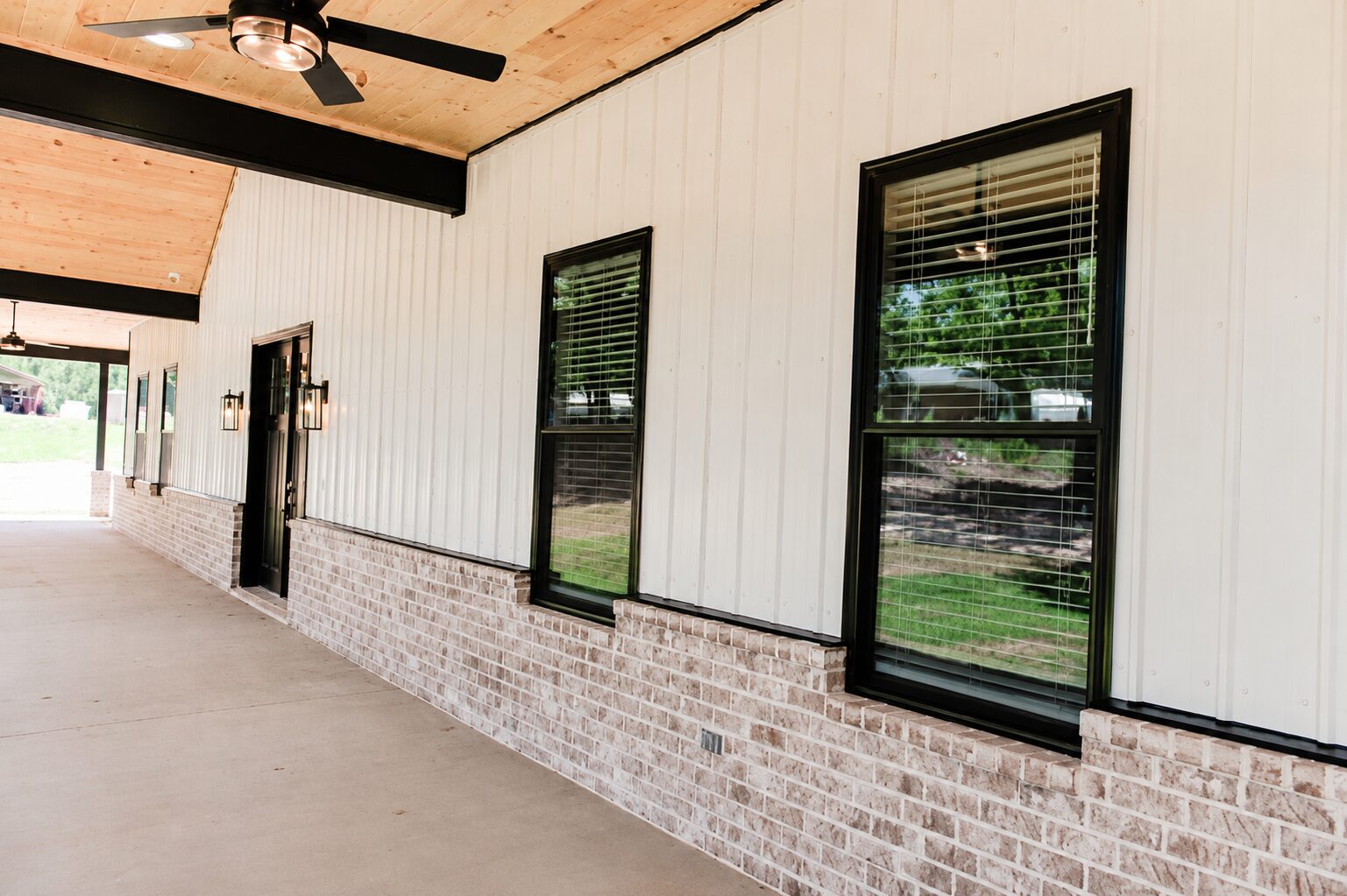 White board-and-batten barndominium porch with brick wainscot and black trim